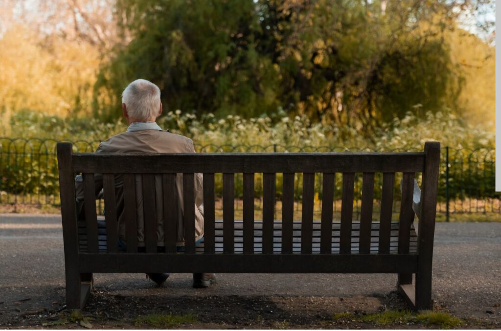 Un hombre anciano aparece solo, sentado en un banco de un parque de cualquier sitio.